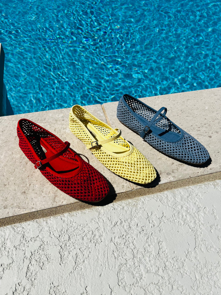 Three colorful shoes (red, yellow, blue) on a ledge by a pool.