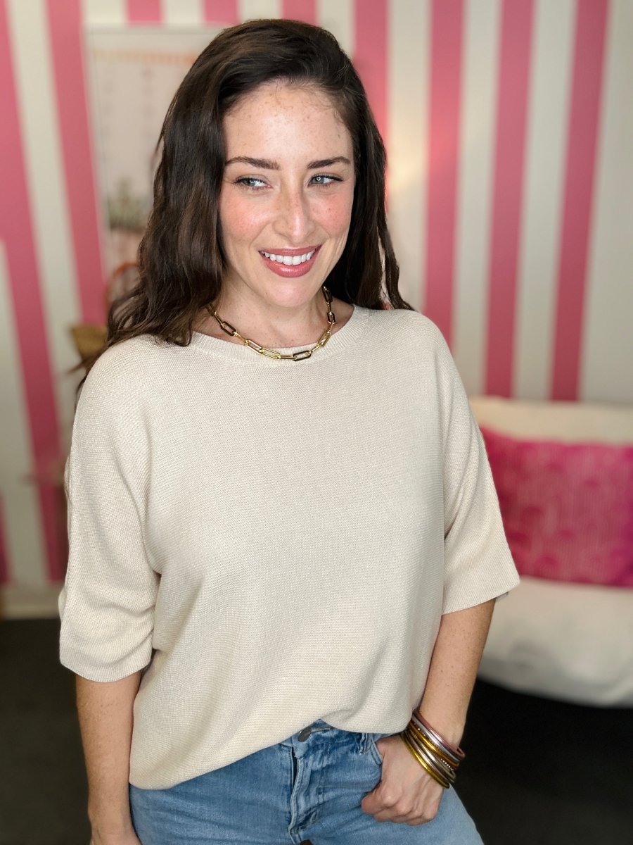 Woman wearing a beige sweater and blue jeans with a striped background