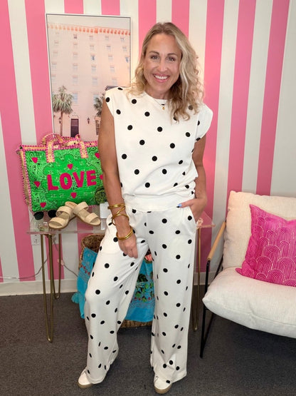 Woman in a polka dot outfit standing in a room with a striped wall and a chair.