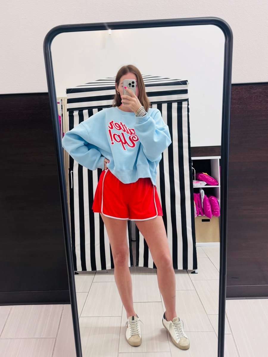 Person wearing a blue sweater with red text and red shorts in front of a mirror.