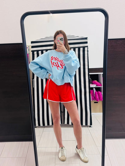 Person wearing a blue sweater with red text and red shorts in front of a mirror.