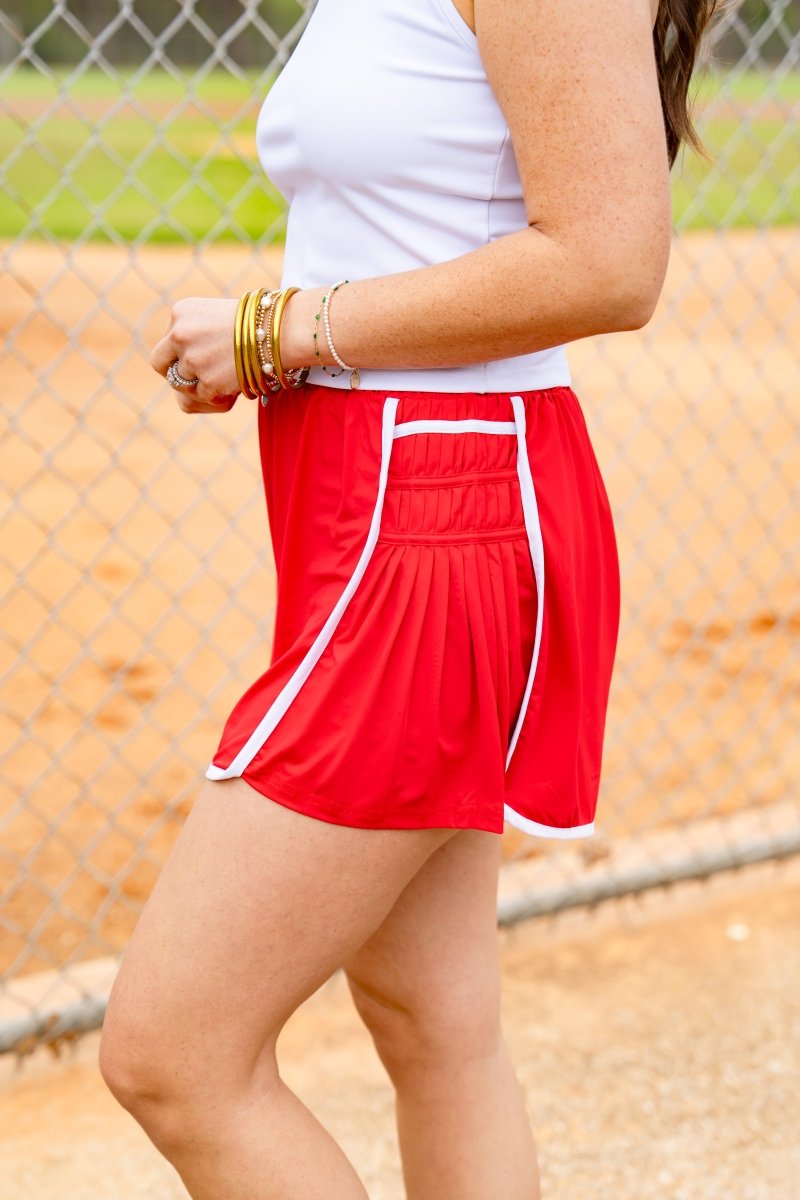 Person wearing a red skirt with white trim on a sports field.