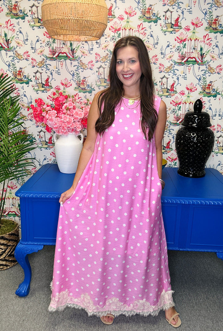 Woman in a pink polka dot dress standing in front of a colorful wall with floral patterns.