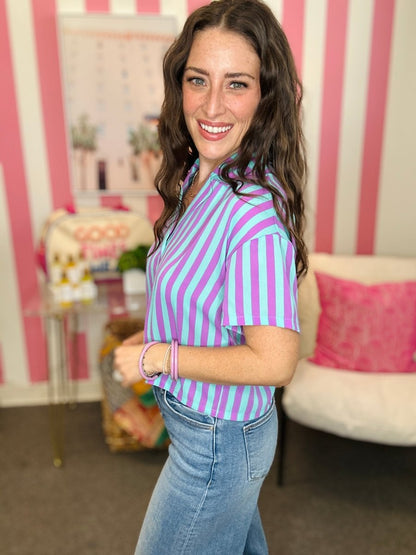 Woman wearing a purple and white striped shirt in a room with pink and white striped walls.