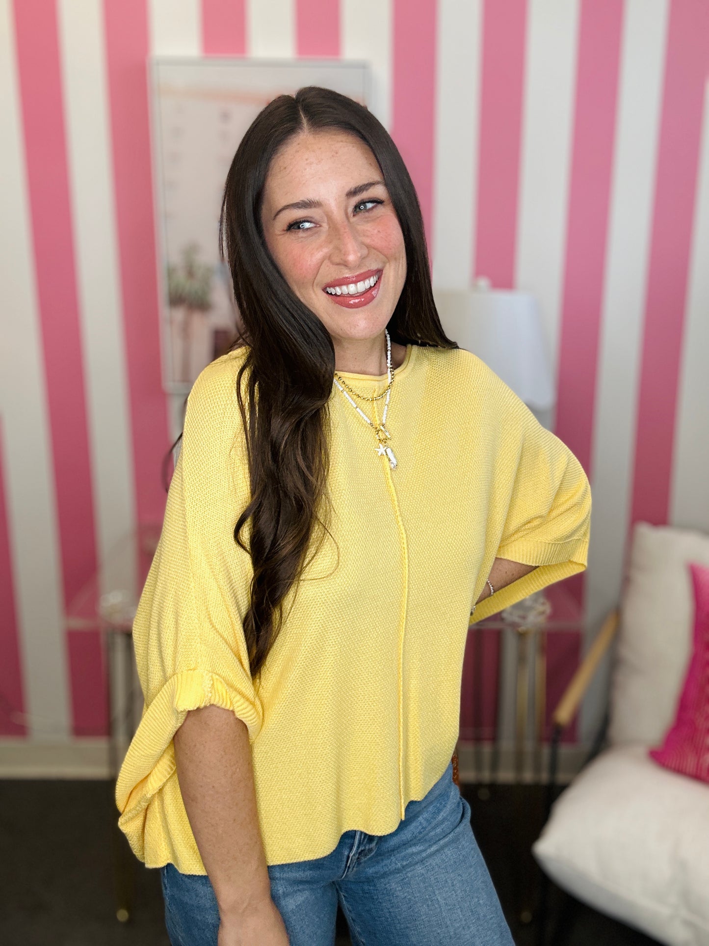Woman wearing a yellow top and blue jeans in a room with pink and white striped walls.