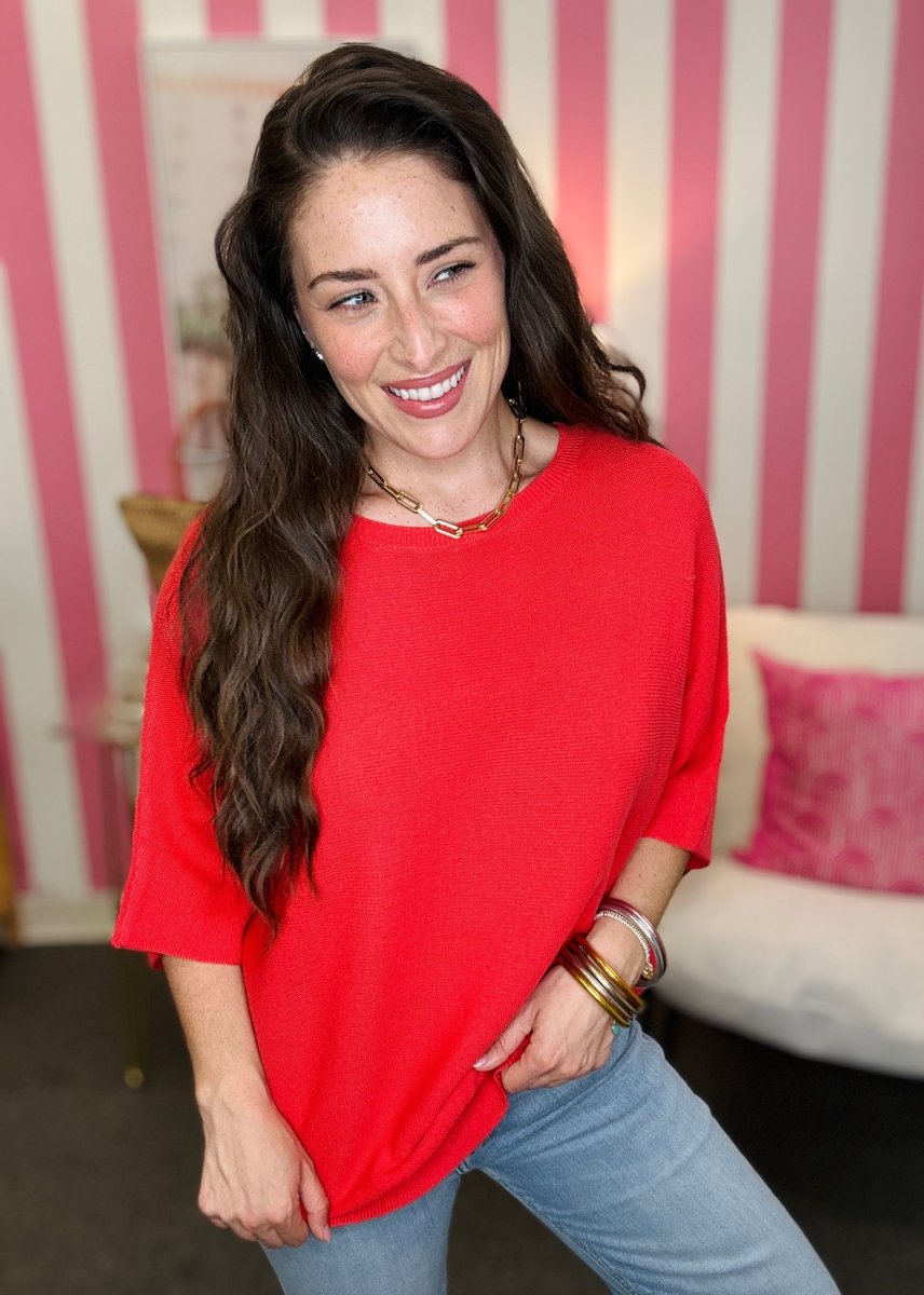 Woman wearing a red top and blue jeans standing in front of a striped wall.