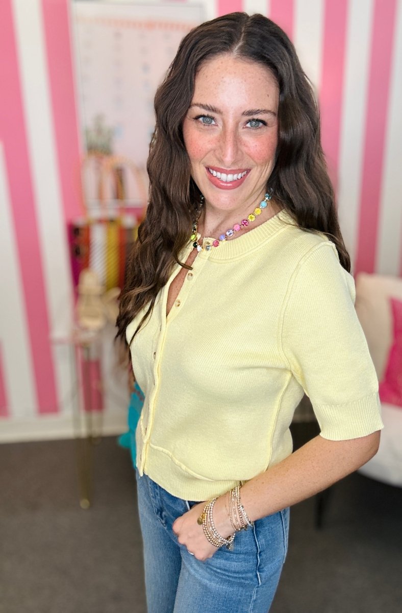 Woman wearing a yellow top and blue jeans in a room with pink and white striped walls.