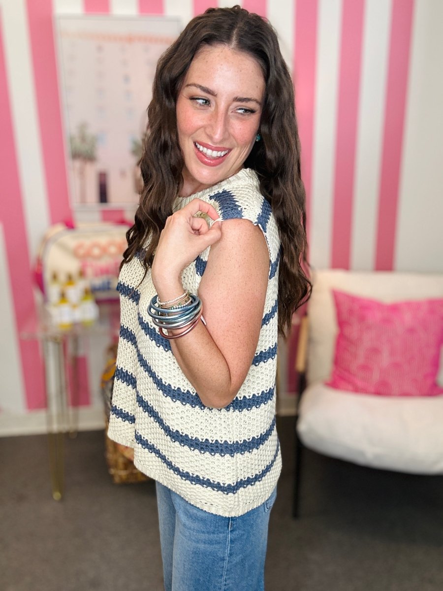 Woman wearing a striped sleeveless top and jeans in a room with pink and white striped walls.