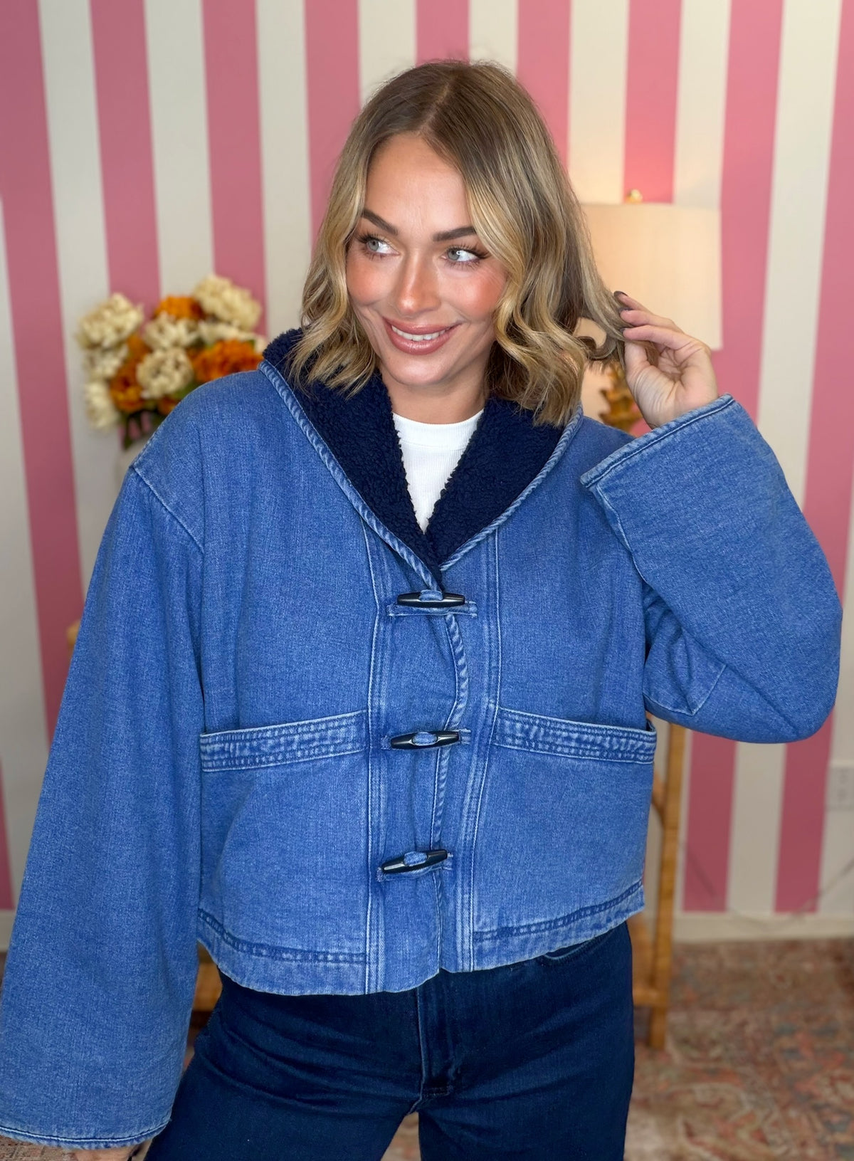 woman standing in a blue denim sherpa jacket in front of a pink striped wall
