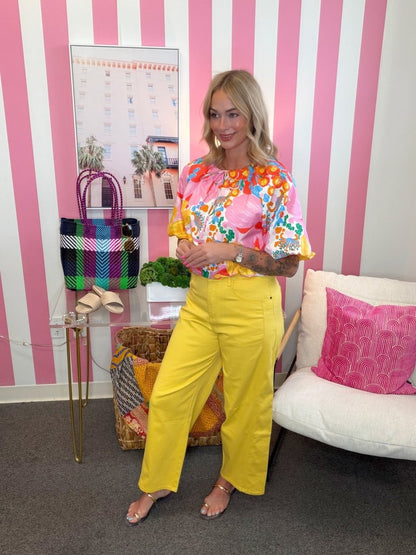 Woman in colorful top and yellow pants standing in a room with pink and white striped walls.