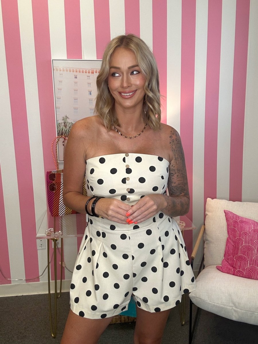 Woman wearing a strapless polka dot dress in a room with pink and white striped walls.