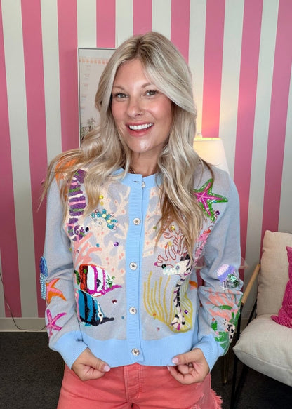 Woman wearing a colorful embroidered jacket in front of a striped wall.