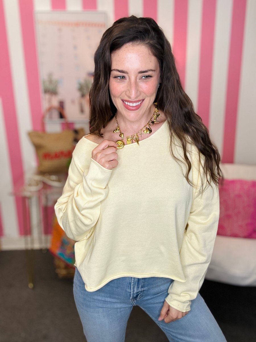Woman wearing a light yellow sweater and blue jeans in a room with pink and white striped wallpaper.