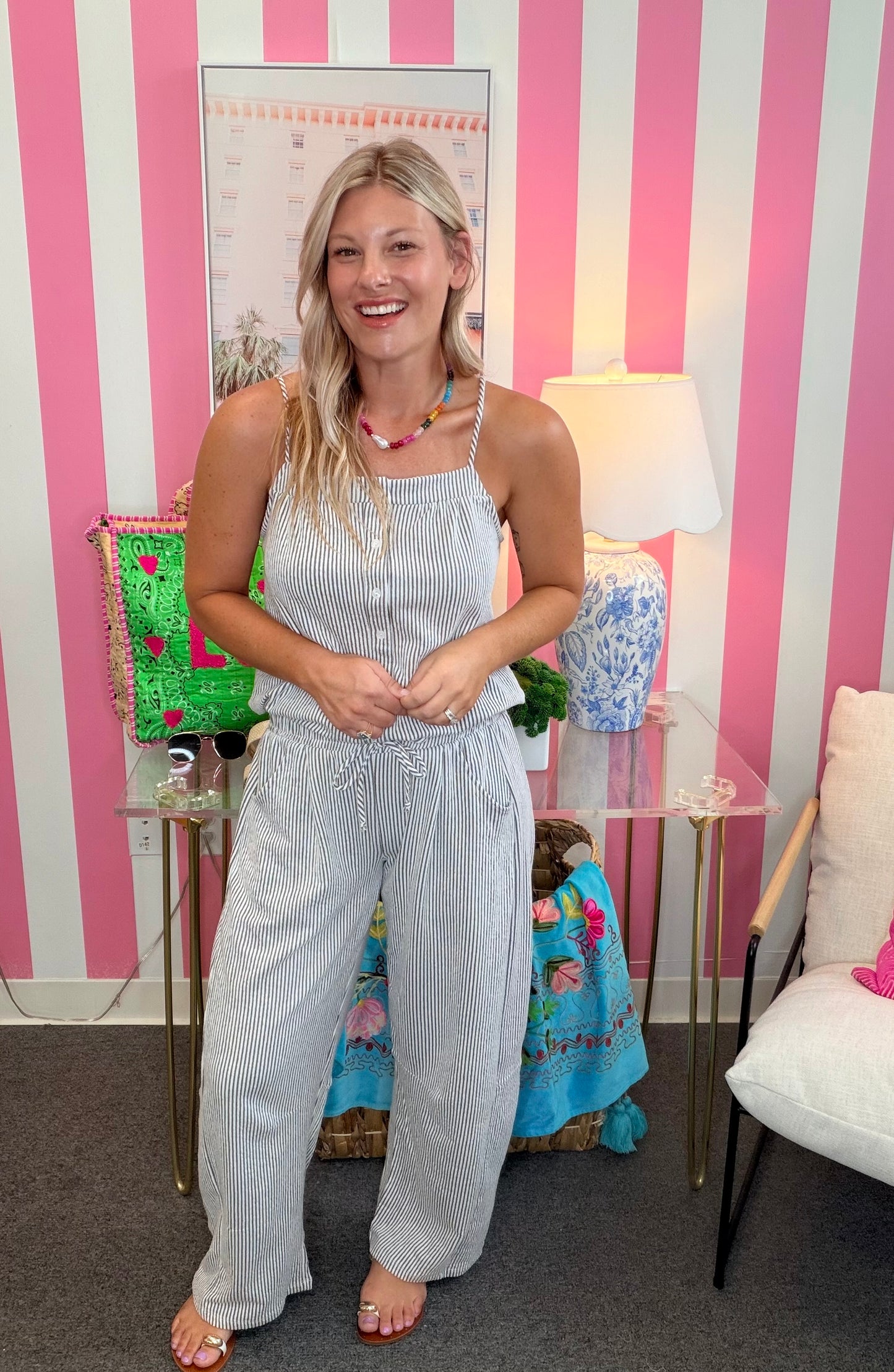 Woman in a light blue striped jumpsuit standing in a room with pink and white striped walls.