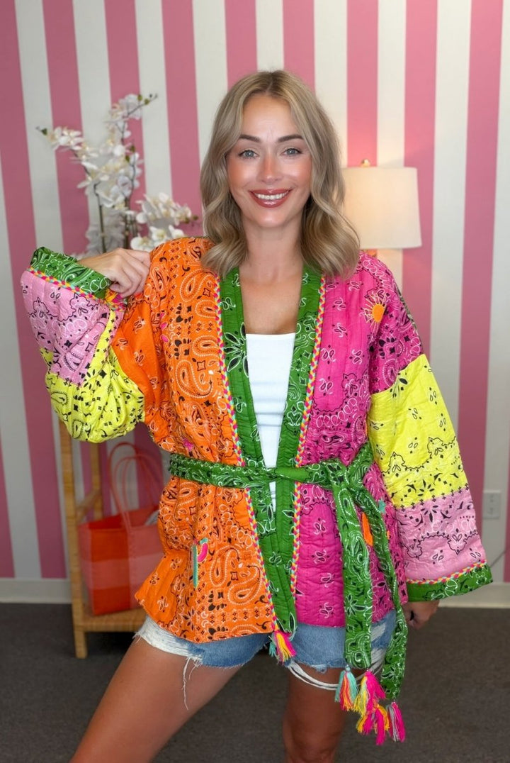 Woman wearing a colorful, patterned kimono in a room with striped wallpaper.