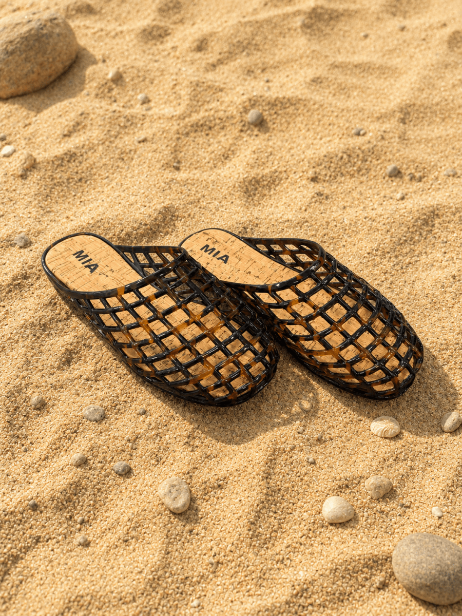 Black woven sandals on a sandy surface with 'MIA' branding.