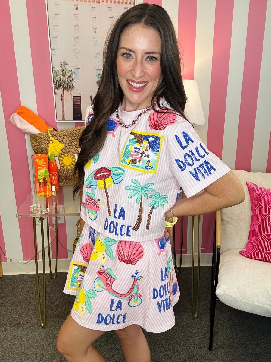Woman wearing a colorful dress with 'La Dolce Vita' text in a room with striped walls.