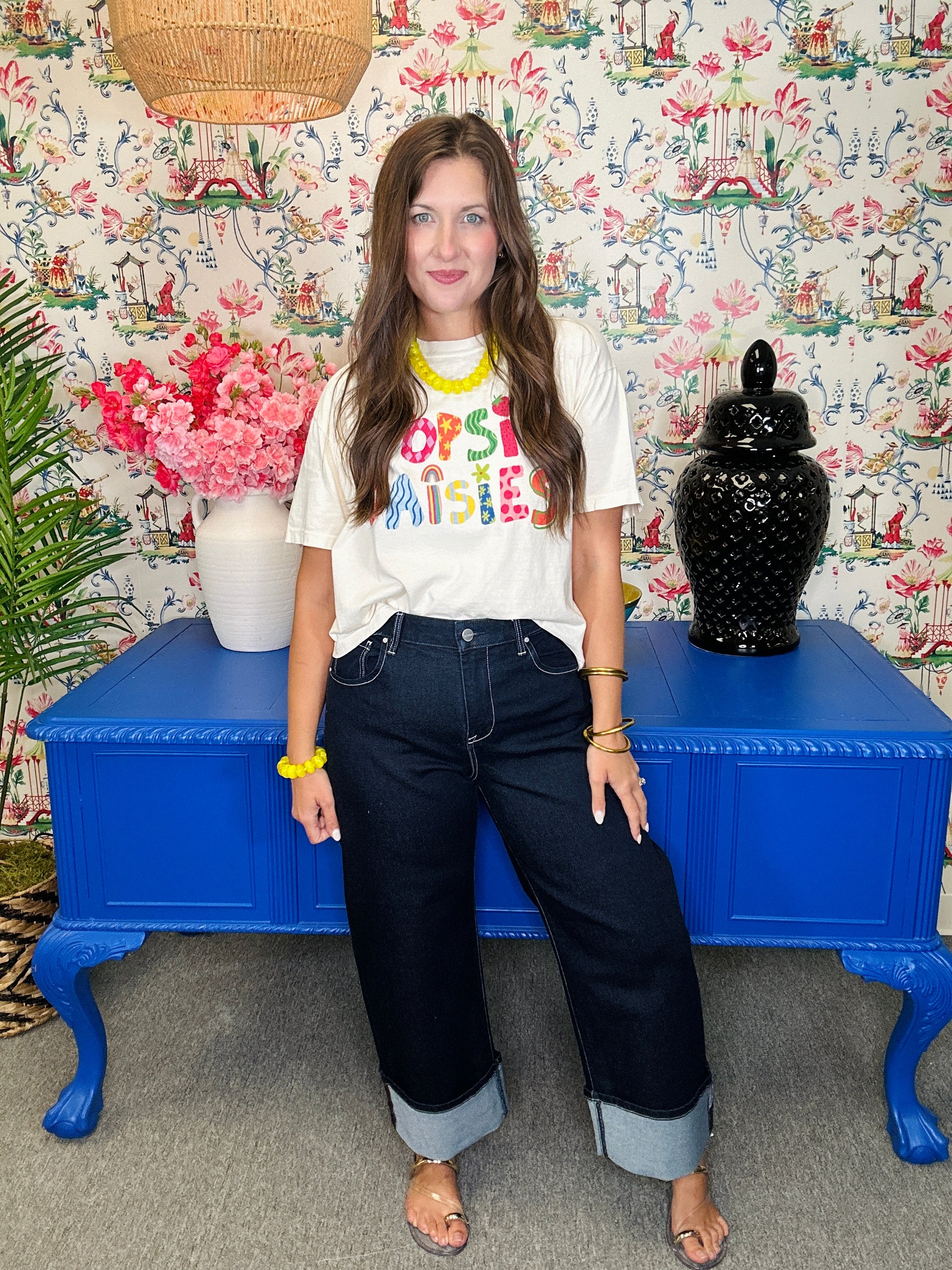 Woman sitting on a blue table with colorful floral and patterned wallpaper in the background