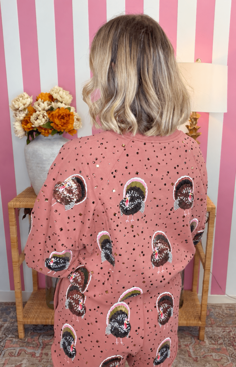 A person viewed from behind wearing a dusty pink sequined tunic top with a black and white patterned print, set against a pink and white striped wall.