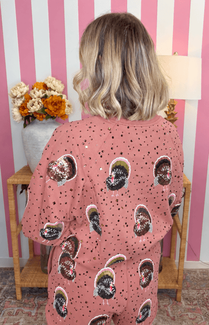 A person viewed from behind wearing a dusty pink sequined tunic top with a black and white patterned print, set against a pink and white striped wall.