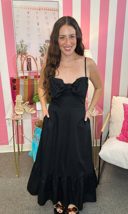 Woman in a black dress standing in a room with striped walls and decorative items.