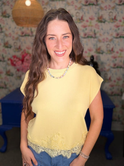 Woman wearing a yellow top with lace details in a room with floral wallpaper.