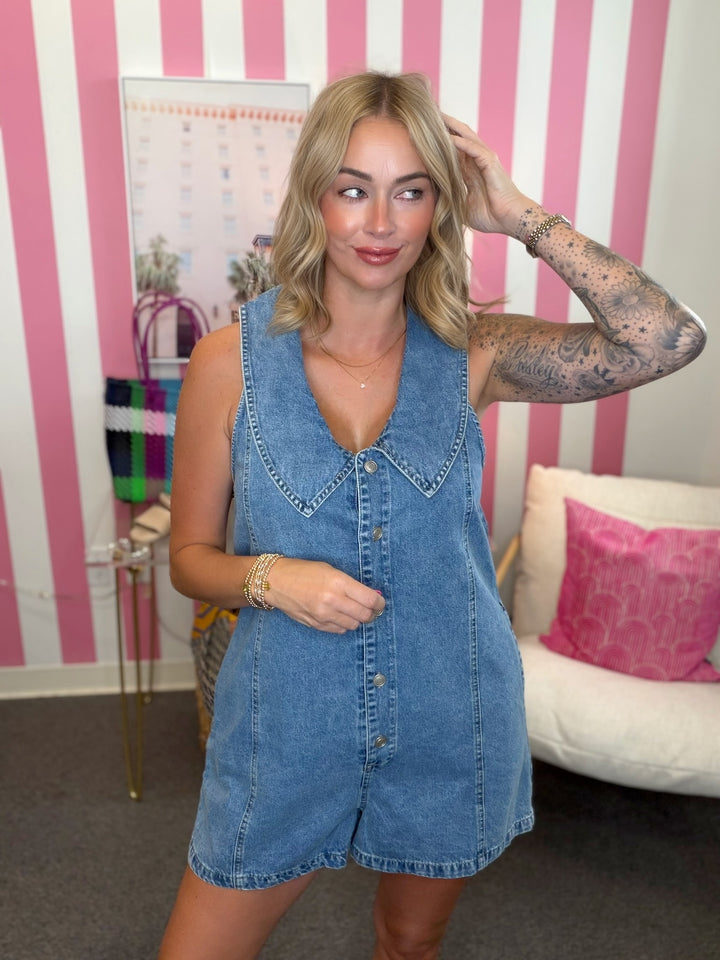 Woman wearing a denim dress in a room with pink and white striped wallpaper.