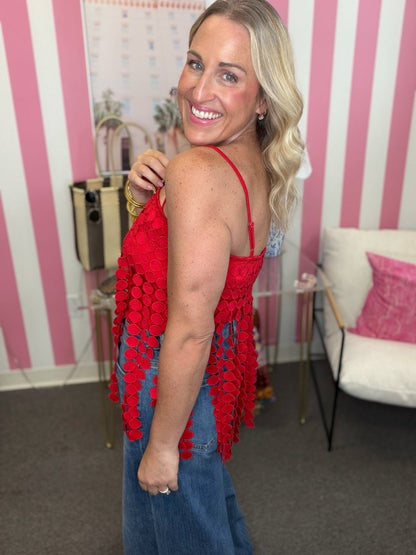 A woman with blonde hair smiling and looking back over her shoulder while wearing a bright red crochet fringed top and blue jeans in a room with pink and white striped walls.