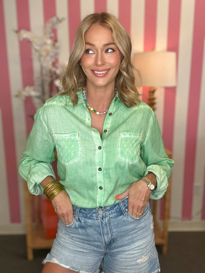 Woman wearing a green shirt and denim shorts in a room with striped wallpaper.