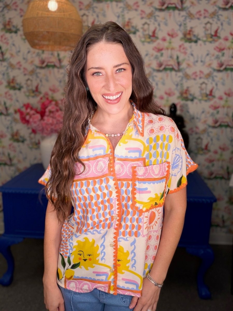 Woman wearing a colorful patterned shirt in a room with floral wallpaper.