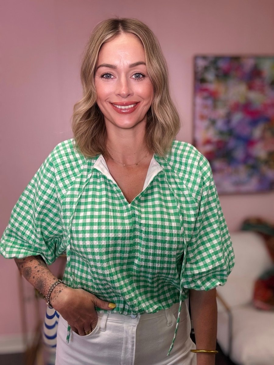 Woman wearing a green and white checkered shirt in a room with a colorful painting on the wall.