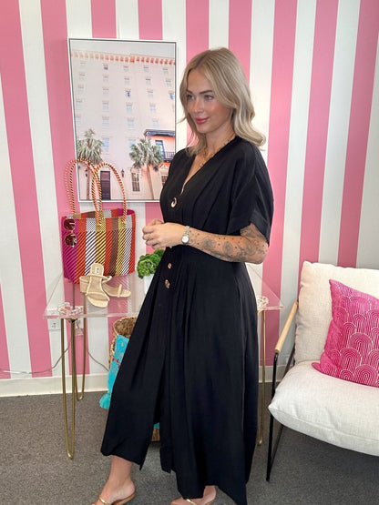 Woman in a black dress standing in a room with pink and white striped walls, holding a green vegetable.