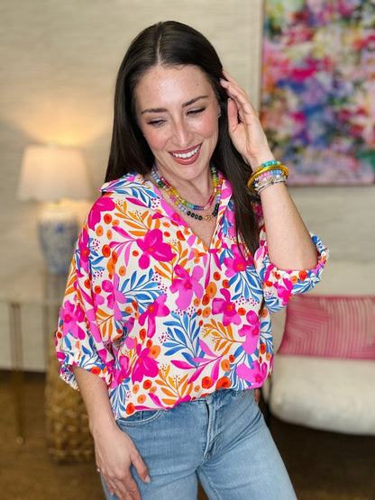 Woman wearing a colorful floral blouse in a room with a lamp and painting.