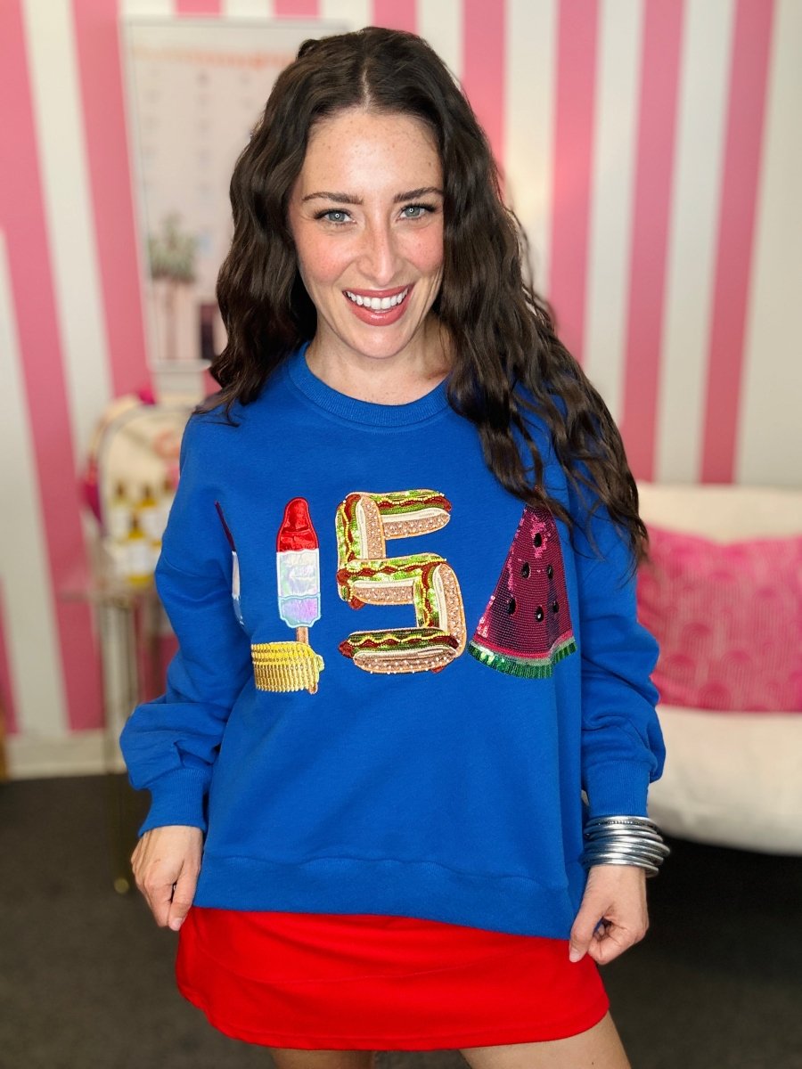 Woman wearing a blue sweatshirt with colorful designs in a room with pink and white striped wallpaper.