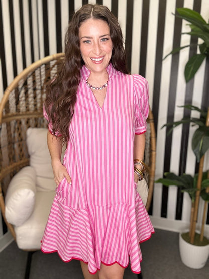 Woman wearing a pink and white striped dress in an indoor setting with a plant and chair.