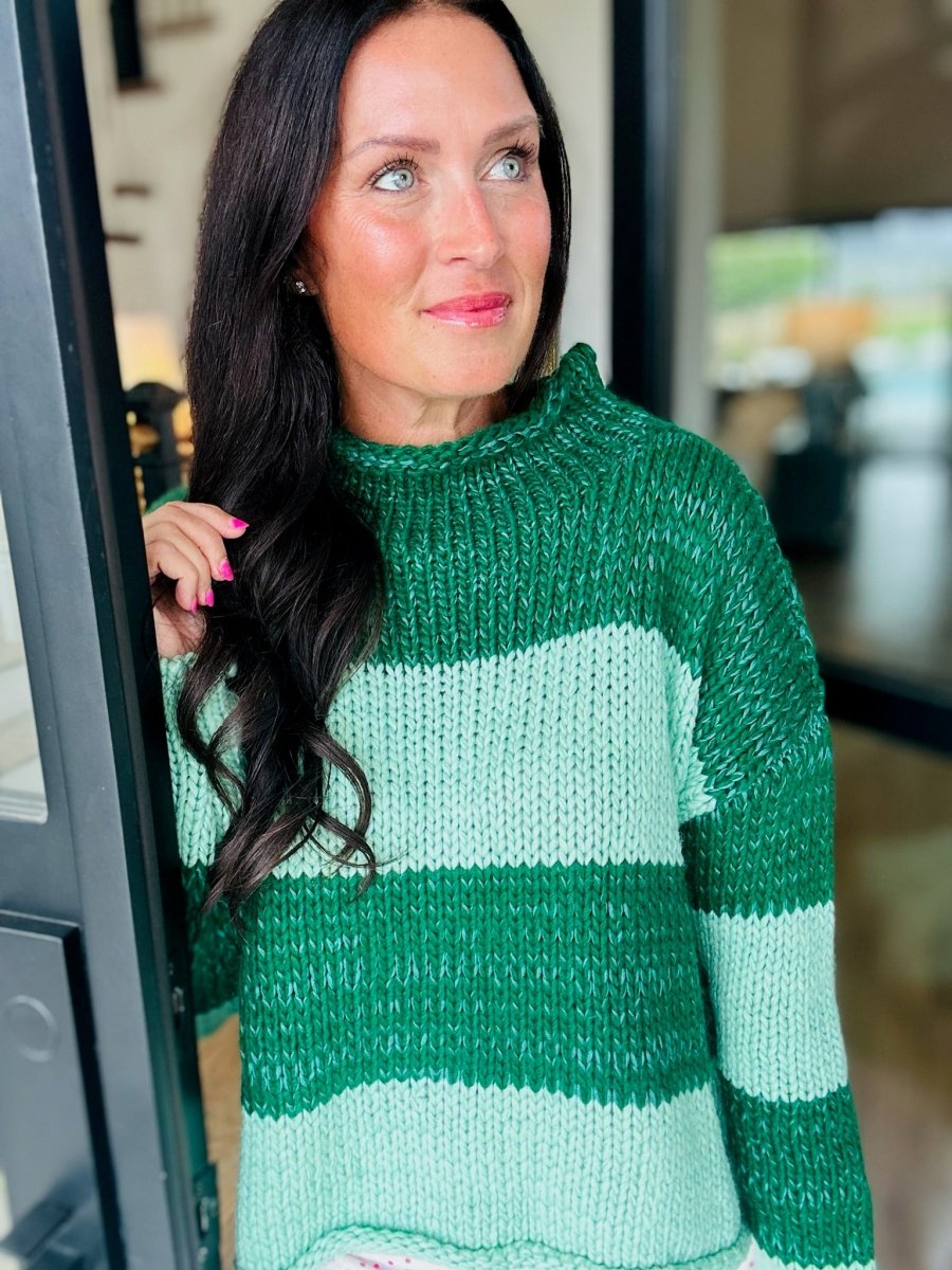 A smiling woman with black hair wearing a chunky knit sweater with green and mint green geometric blocks.
