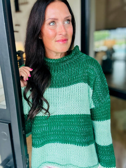 A smiling woman with black hair wearing a chunky knit sweater with green and mint green geometric blocks.