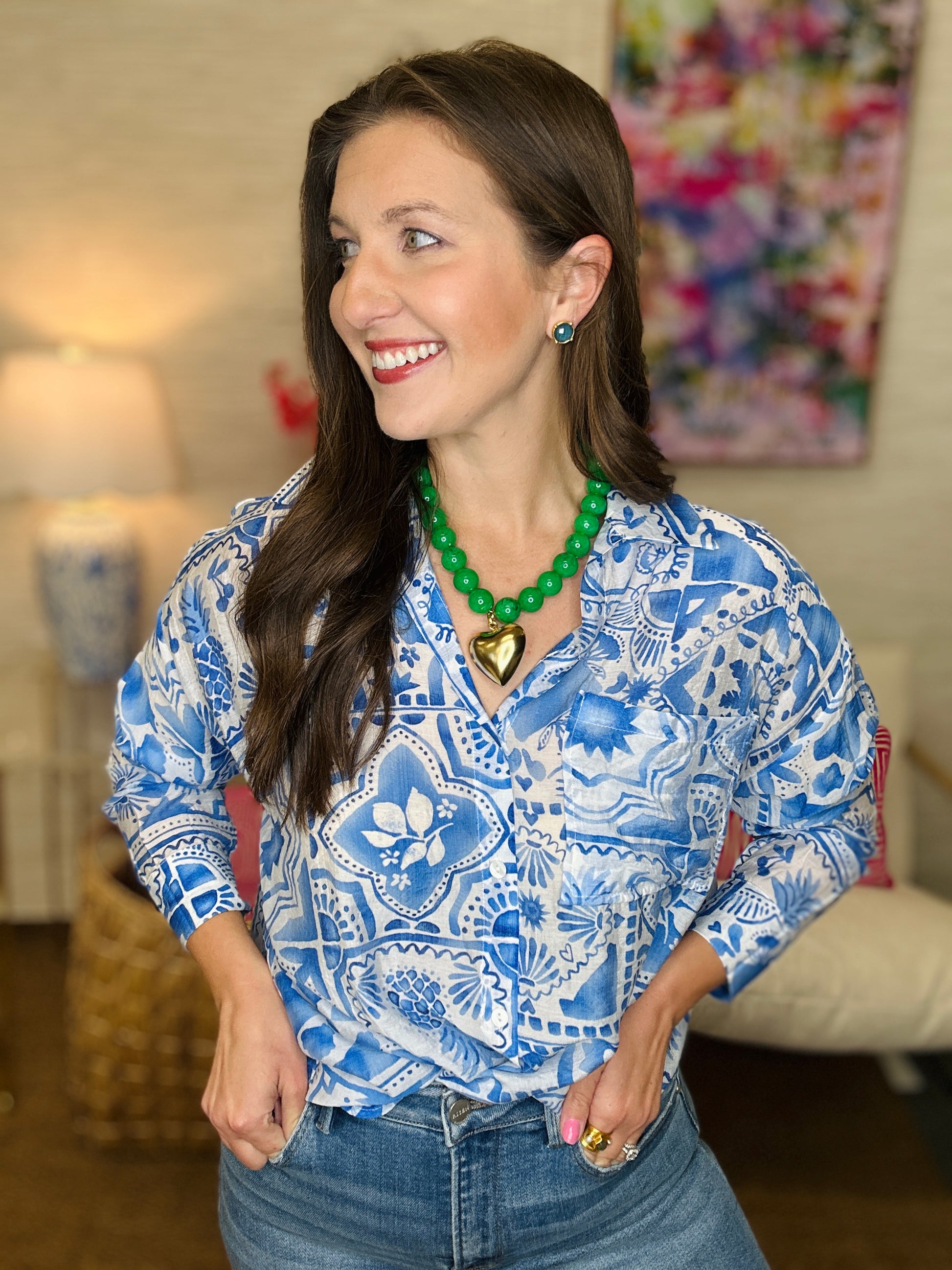 Woman wearing a blue patterned blouse and green necklace in a room with colorful artwork.