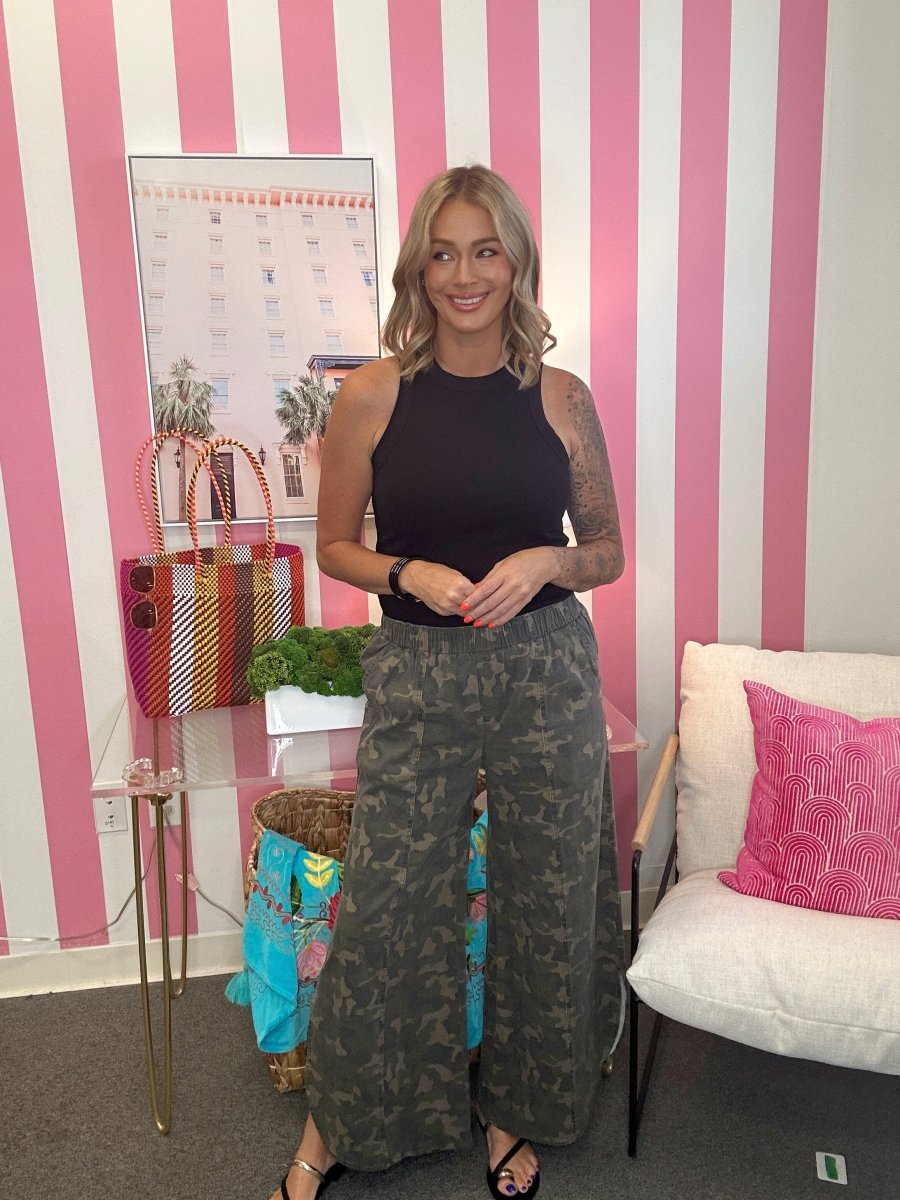Woman standing in a room with pink and white striped walls, holding a colorful handbag.