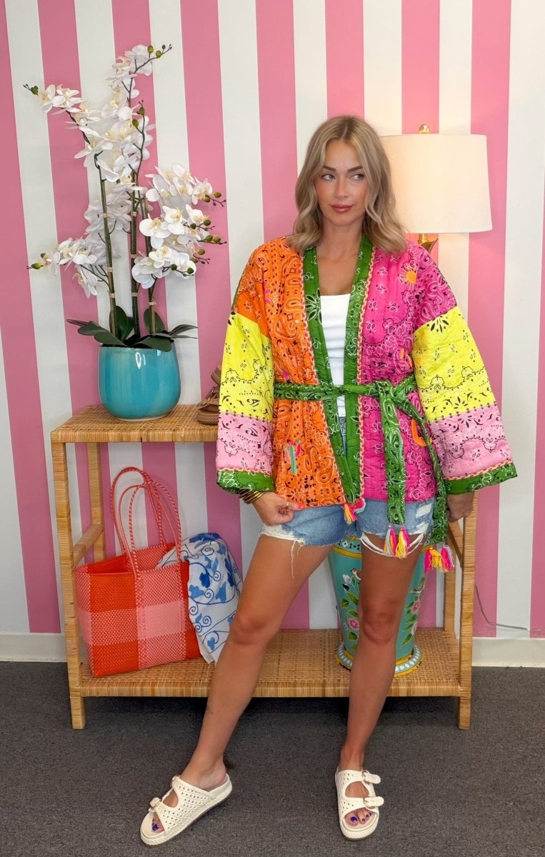 Woman wearing a colorful kimono-style jacket in a room with striped walls and a lamp.