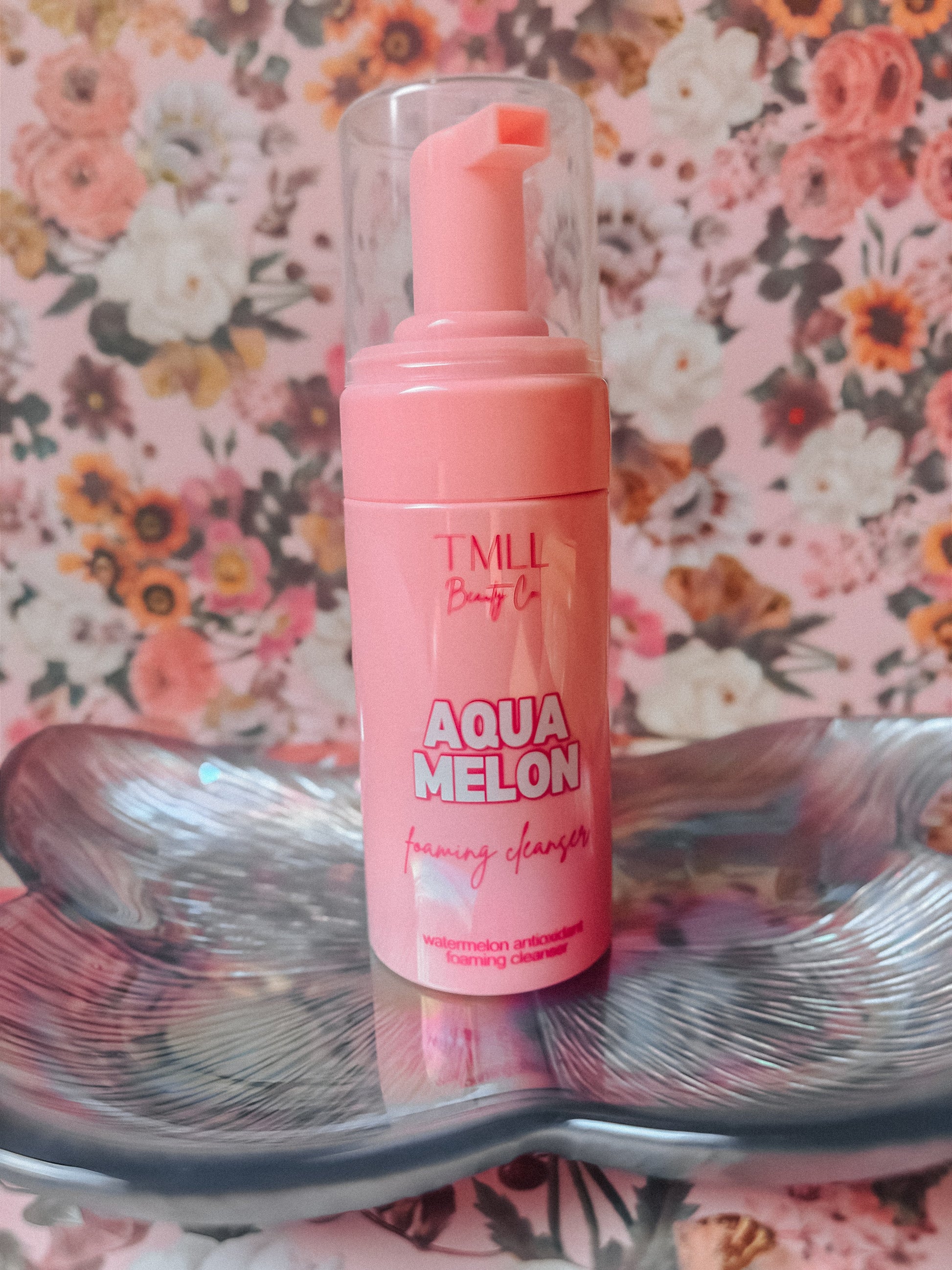 Pink bottle labeled 'Aqua Melon' on a decorative plate with floral background