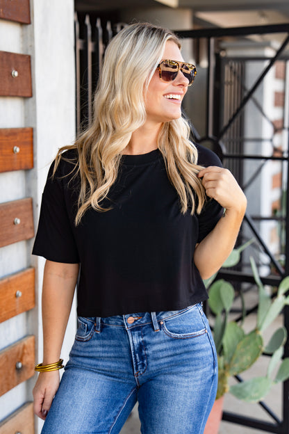 Woman wearing a black t-shirt and blue jeans standing outdoors.