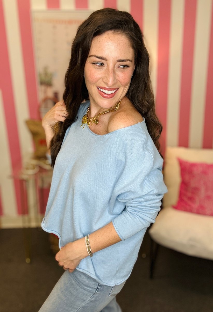 Woman wearing a light blue off-shoulder top in a room with striped wallpaper.