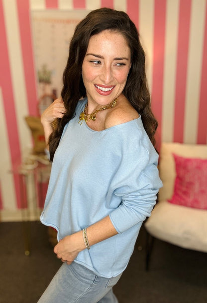 Woman wearing a light blue off-shoulder top in a room with striped wallpaper.