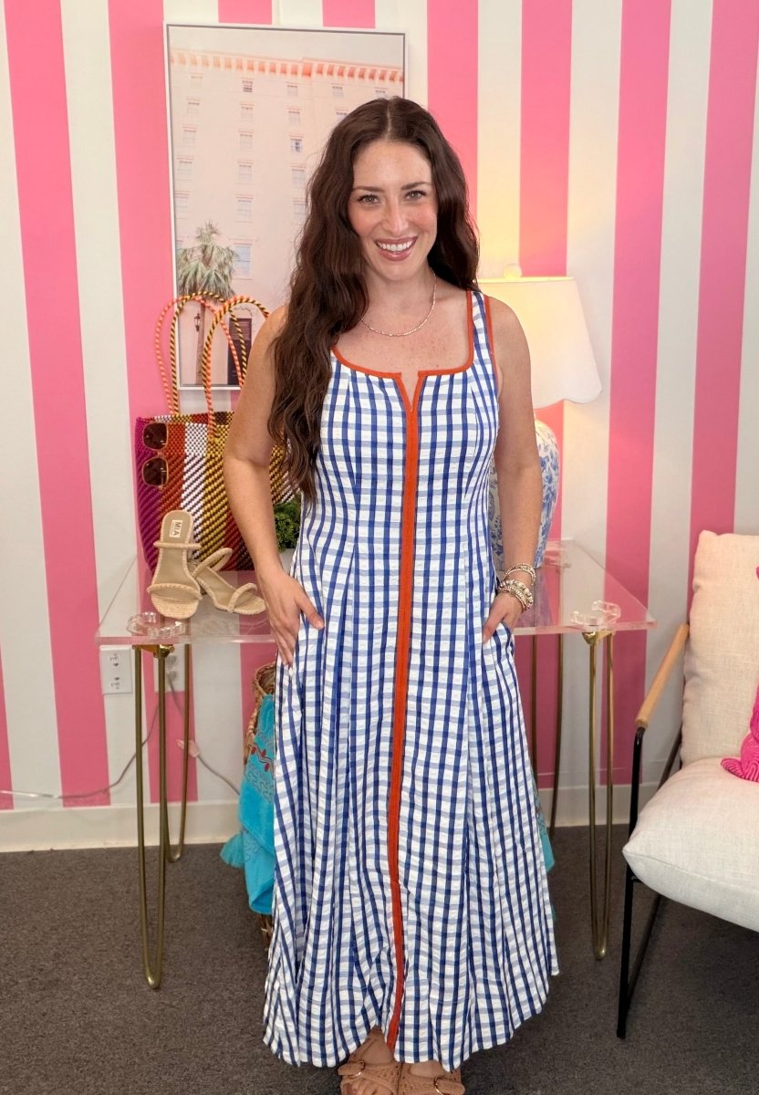Woman in a blue checkered dress standing in a room with striped walls and furniture.