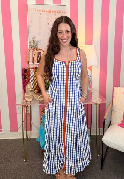 Woman in a blue checkered dress standing in a room with striped walls and furniture.