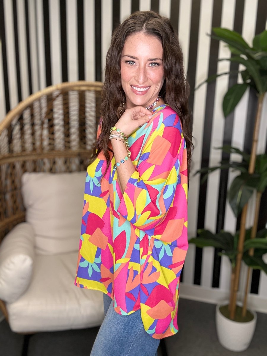 Woman wearing a colorful patterned top in a room with a couch and plant.