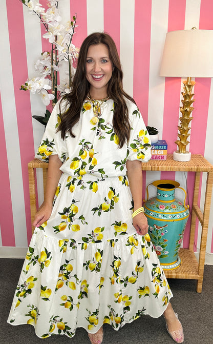Woman wearing a white dress with yellow lemon print in a room with pink and white striped walls.