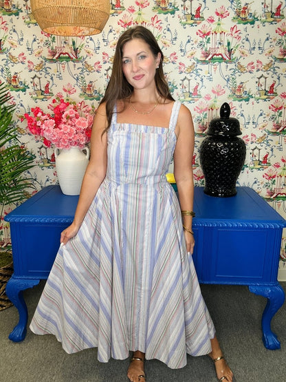 Woman in a striped dress standing in front of a colorful wall with floral patterns and blue furniture.