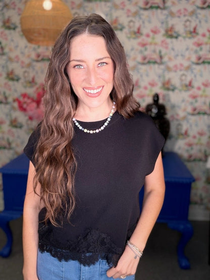 Woman wearing a black top with lace details in a room with floral wallpaper.